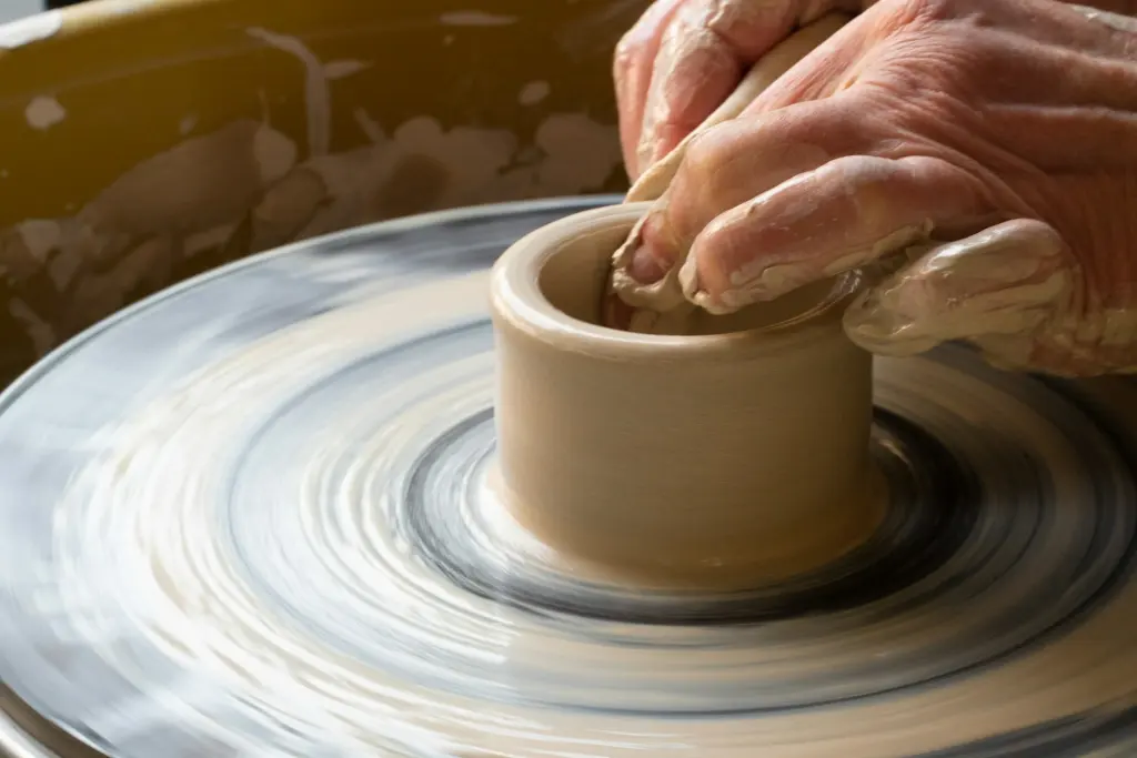 A potter's hands shaping a stoneware pot on the wheel