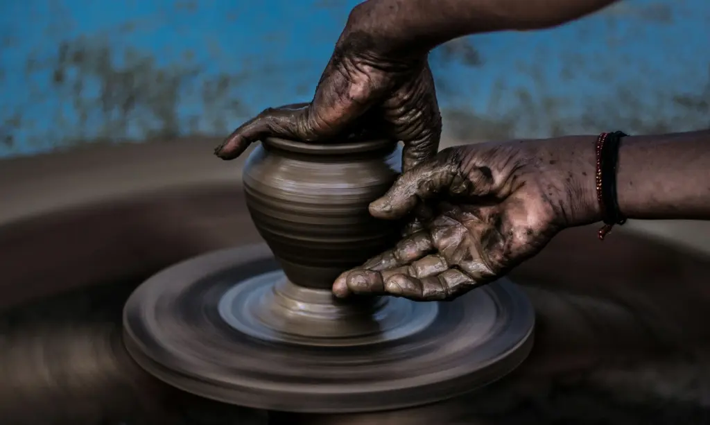 Hands pulling up the wall of a pot on the wheel